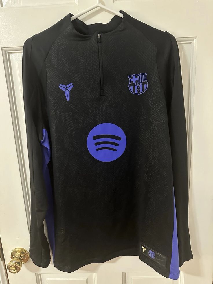Black long-sleeve shirt with logos on a hanger against a white door background