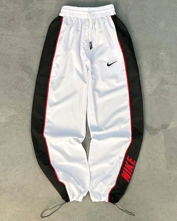White and black Nike tracksuit pants with red accents on a gray surface